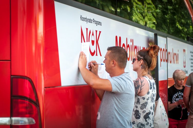 Zdjęcie - ludzie wypełniają ankiety, opierając kartki o autobus krwiodawstwa