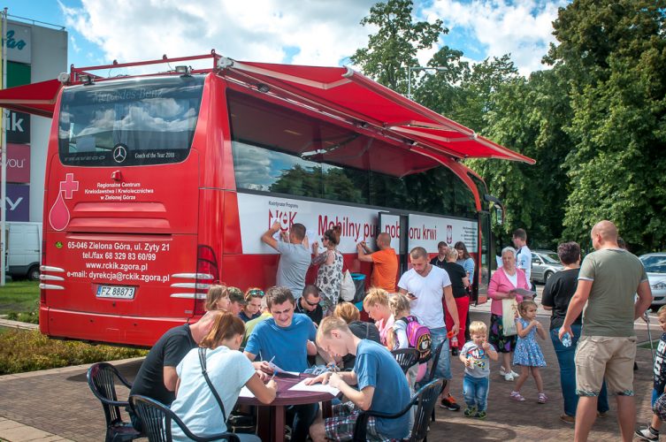 Zdjęcie w dalszym planie - osoby wypełniają ankiety przed autobusem krwiodawstwa