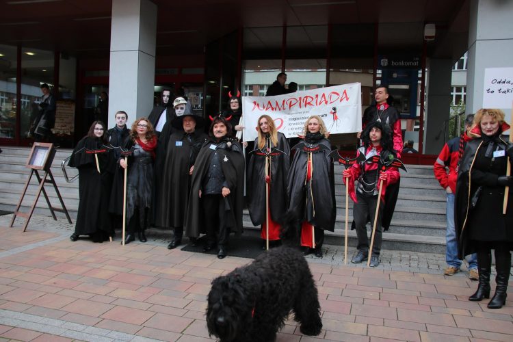 Zdjęcie: ludzie przebrani za wampiry i czarny kudłaty pies na pierwszym planie