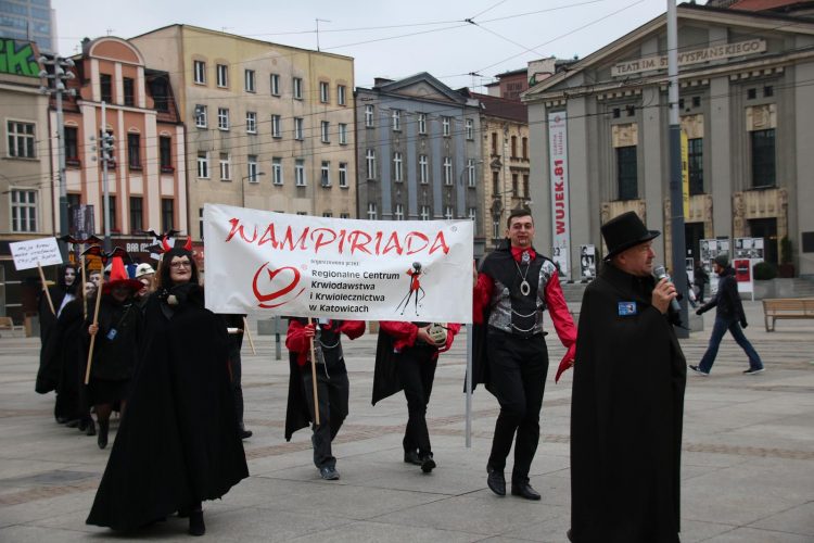 Zdjęcie: osoby przebrane za wampiry trzymają plakat wydarzenia